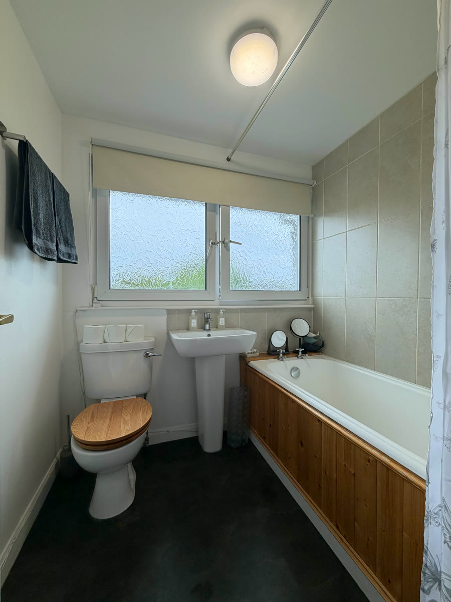 Bathroom with bath and shower in Inverness holiday let — toilet, sink, tiled walls